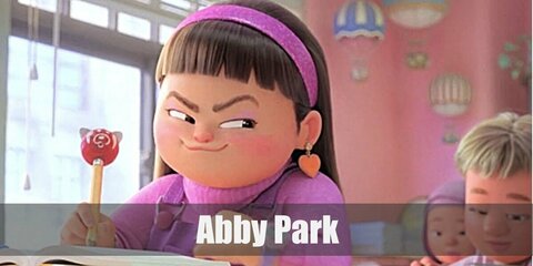 Abby's purple ensemble features a turtleneck, an overall, and maroon shoes. For her accessories, she wears  rainbow band, a watch, and heart earrings, too. 