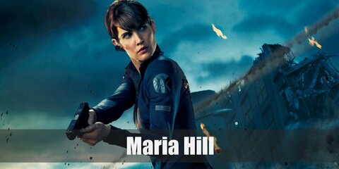 Maria Hill's costume features a golf jacket and skinny pants. She wears a pair of shin guards, boots,and a gun holster. She also wears her hair in a ponytail.