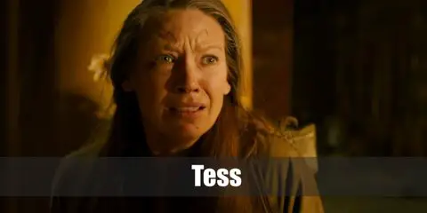 Tess’s costume is a short-sleeved black shirt blouse, mid-wash boot-cut jeans, black work shoes, a short-sleeved red wine button-down shirt, and a printed bandana headband.