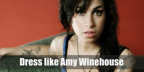 Amy Winehouse costume is a white tank top with a black bra peeking over the top, low sitting blue shorts, large hoop earrings, and red slip on sandal shoes.