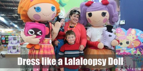  Lalaloopsy costume is a polka-dotted top, an orange tutu, black and white-striped tights, and a pair of pink boots. She also has purple yarn hair, tied back into two ponytails using red ribbon.
