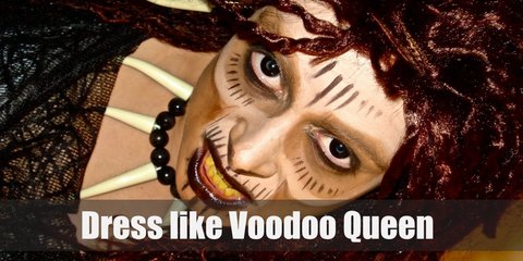 Voodoo queen costume is a red corset topped with a Victorian long coat, black leggings, high heel boots, a dreadlock wig, a top hat, a day of the dead half-face mask, leather and bead bracelets, a bone necklace and belt, and a dark fabric also as a belt.
