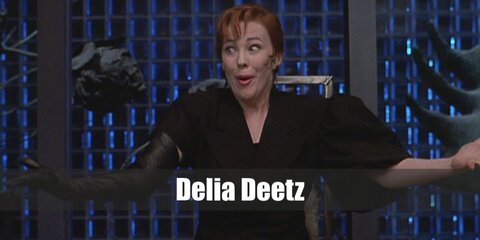 Delia Deetz' costume features a long black dress, one glove on her arm, and a ginger-colored wig styled with a headband.