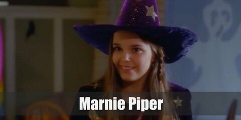 Marnie's costume features a red top wih skirt and boots. She styles it with a crossbody bag and a velvet cape. Top the costume off with a vintage book and a purple wizard's hat.