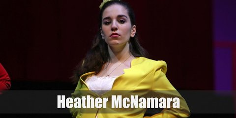 Heather McNamara’s costume is a yellow blazer, a yellow plaid skirt, a black bow belt, yellow knee-high socks, and yellow Mary Janes. 