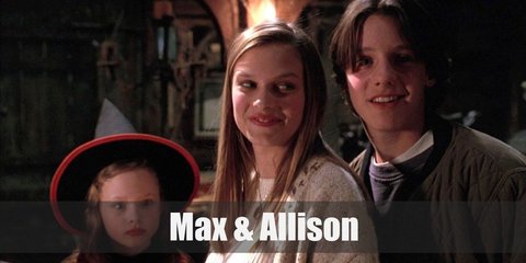 Max’s costume is a blue sweatshirt, denim pants, and a bomber jacket. Allison’s costume is a white sweater, a beige cardigan, and denim jeans. 