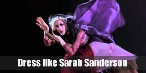 Sarah Sanderson costume has beautiful wavy blond hair and a Gothic-styled makeup. She also has a lot of rings and a gold necklace. Her outfit includes a red medieval gown and a long purple cloak.