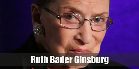 Ruth Bader Ginsburg’s costume is her black Court robes, green earrings, a thick necklace, black-rimmed glasses, and her hair on a bun.