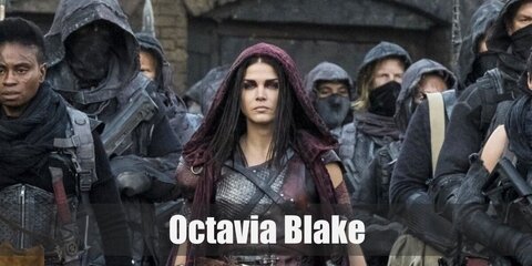 Octavia Blake wears her corset with a belt and dark pants. She also has a pair of boots and a brown cape over her costume. She carries a toy sword, too.