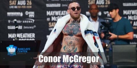  Conor McGregor’s costume is a pair of purple paisley pants, a white faux fur coat over his tattoos, and a pair of dark sunglasses.